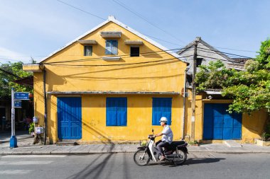 Hoi An, Vietnam - Haziran 2019: Eski şehirde renkli evin yanında scooter kullanan adam