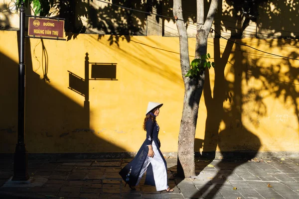 Хойан, Вьетнам - июнь 2019 года: Вьетнамская женщина, идущая вдоль желтой стены в старом районе города Стоковое Фото