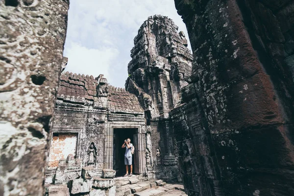 Hombre caucásico con cámara de pie entre las ruinas del complejo de templos Angkor Wat en Siem Reap, Camboya —  Fotos de Stock