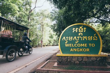 Siem Reap, Kamboçya - Haziran 2019: Angkor Wat tapınağına giden motosiklet çekçeki karşılama tabelasını geçiyor