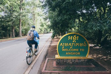 Siem Reap, Kamboçya - Haziran 2019: Angkor Wat tapınağına bisikletle geçen kadın karşılama tabelasını geçiyor