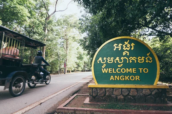Siem Reap, Kamboçya - Haziran 2019: Angkor Wat tapınağına giden motosiklet çekçeki karşılama tabelasını geçiyor