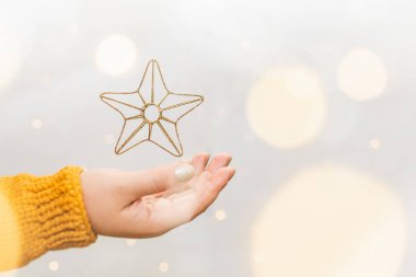 Altın Noel yıldızı turuncu kazak kadın el üzerinde levitating, arka planda çelenk bokeh