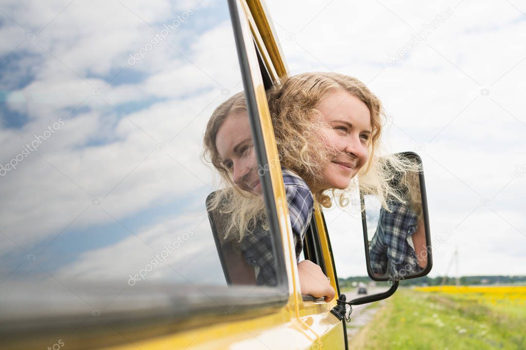 Portrait of blonde Caucasian woman through car window with sunflower field on background