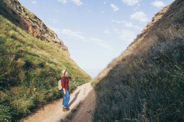 Sırt çantalı bir kadın, deniz manzaralı dağ kanyonunda yürüyüş yapıyor.