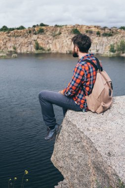 Sırt çantalı bir adam dağda yürüyüş yapıyor. Uçurumun kenarında duruyor ve kayalık kanyona bakıyor.