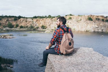Sırt çantalı bir adam dağda yürüyüş yapıyor. Uçurumun kenarında duruyor ve kayalık kanyona bakıyor.