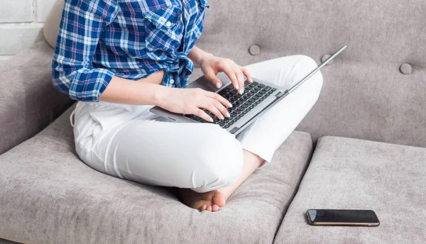 Jovem mulher sentada em um sofá com computador portátil em casa — Fotografia de Stock