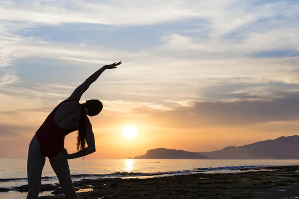 Jovem praticando ioga na praia durante o pôr do sol — Fotografia de Stock