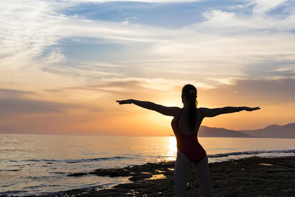 Silhueta mulher saudável fazendo exercícios de Yoga na praia ao pôr do sol, Tailândia . — Fotografia de Stock