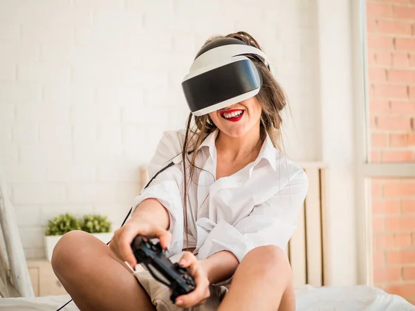 Young female gamer in wearable VR headset playing action 3d video game at home, excited teen holding wheel and screaming driving digital racing car in simulator application