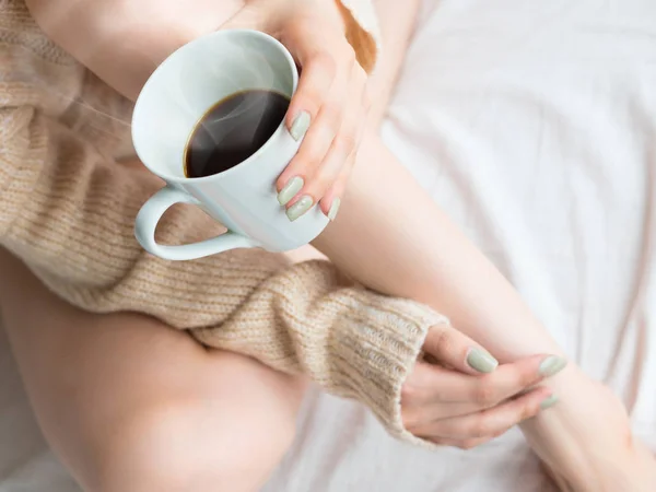 Foto de piernas y manos femeninas relajándose y bebiendo café en la cama . — Foto de Stock