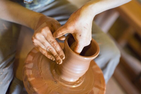 Rotating potters wheel and clay ware on it vase : taken from above. Hands in clay. Pottery: male ceramist creates a hand made clay product. Process of rotation of potters wheel, hands of ceramist.