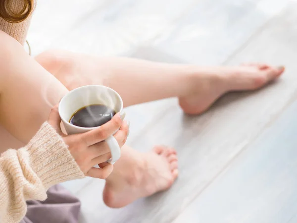 Mujer joven se relaja en casa y bebe café fragante. Hermoso primer plano de los pies femeninos. foto recortada humana irreconocible — Foto de Stock