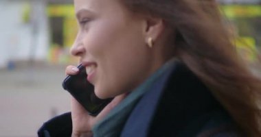 Çekici ve neşeli genç kadın dışında bir cep telefonu kullanarak. O telefonda konuşurken ve gülüyor. Kalabalık şehir sokak. Yakın çekim.