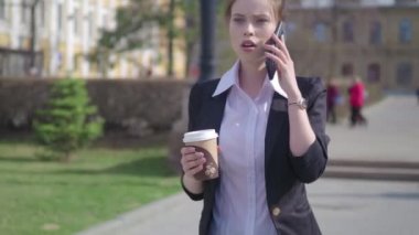 Bir kahve tutan bir kat konuşma telefonda, giyen ciddi bir kadın portresi. arka plan bulanık sokakta