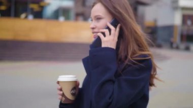 İş kadını kullanma Smartphone kentin çekici esmer. Güzel genç iş kadını konuşarak telefon ve içme kahve