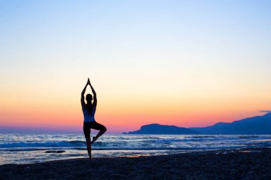 Genç sağlıklı kadın gün batımında plajda yoga yapıyor.