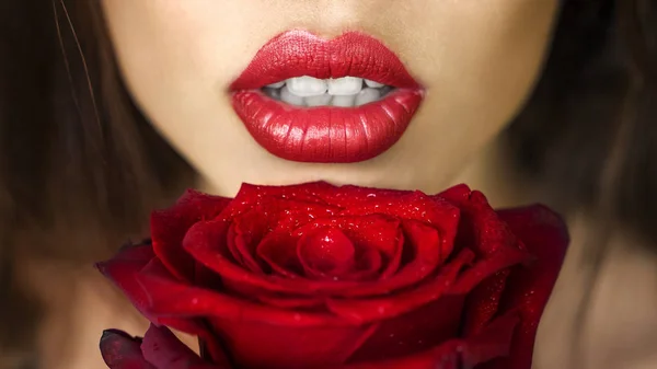 Close-up beautiful female lips with bright red makeup. Perfect clean skin, sexy lip make-up. Beautiful spa portrait with tender red rose flower. — Stock Photo, Image