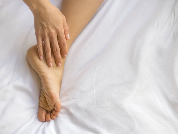 Młoda kobieta masuje jej stopy na łóżku. Pojęcie opieki zdrowotnej — Zdjęcie stockowe