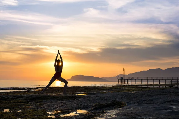 Jovem praticando ioga na praia durante o pôr do sol — Fotografia de Stock