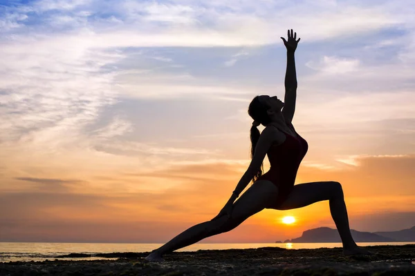 Silhueta mulher saudável fazendo exercícios de Yoga na praia ao pôr do sol — Fotografia de Stock