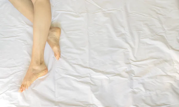 Kvinnliga ben i sängen se ovanifrån, vita sängkläder — Stockfoto