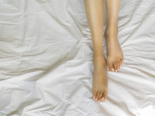 Female legs in bed view from above, white bedding — Stock Photo, Image