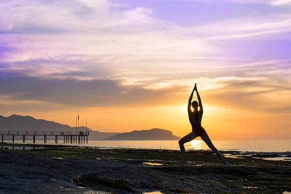Jovem mulher saudável praticando ioga na praia ao pôr do sol — Fotografia de Stock