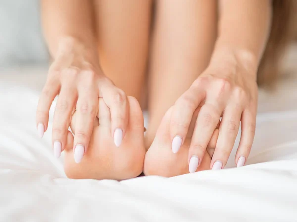 Woman Holding her Tired Feet in Hand Sitting on Bed with White Sheets. — Stock Photo, Image