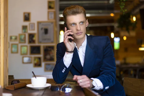 Närbild porträtt av allvarliga stilig man talar på smartphone och sitter vid bord i café. Framifrån. — Stockfoto