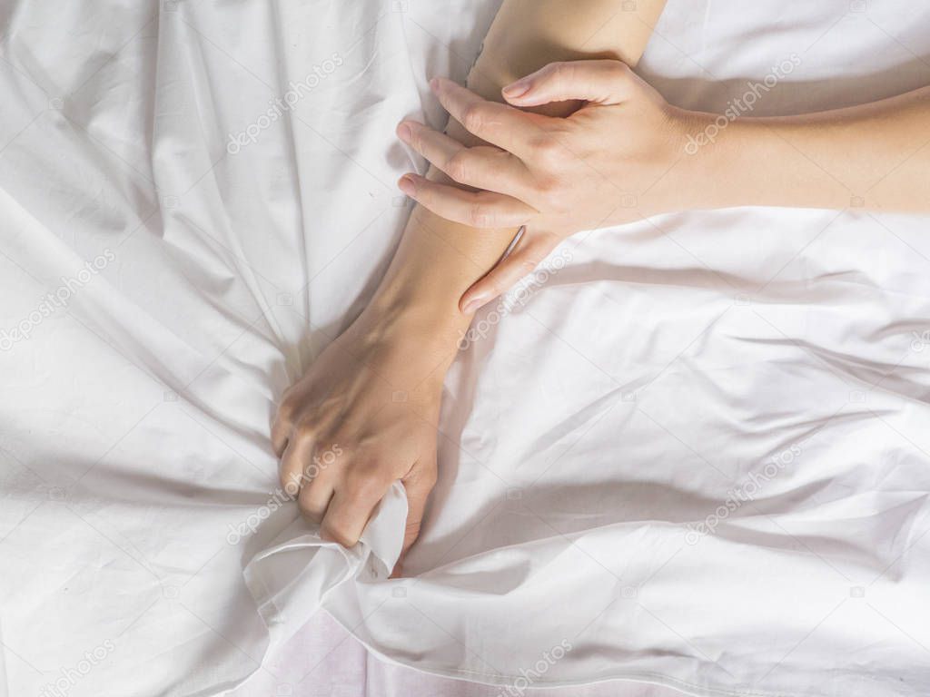 Hand clutches grasps a white crumpled bed sheet in a hotel room, a sign of ecstasy, feeling of pleasure or orgasm. Orgasm is the greatest point of sexual pleasure or a climax of sexual excitement.