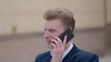 Yakışıklı genç iş adamı bir klasik takım elbise ve ceket iş bölgesi sokaklarında yürüyüş akıllı telefon üzerinde konuşuyor