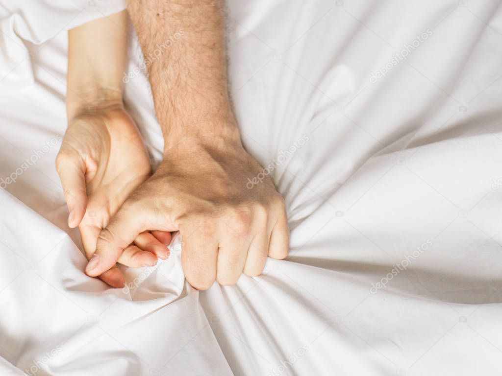 Couple having sex. Hand clutches grasps a white crumpled bed sheet in a hotel room, a sign of ecstasy, feeling of pleasure or orgasm.