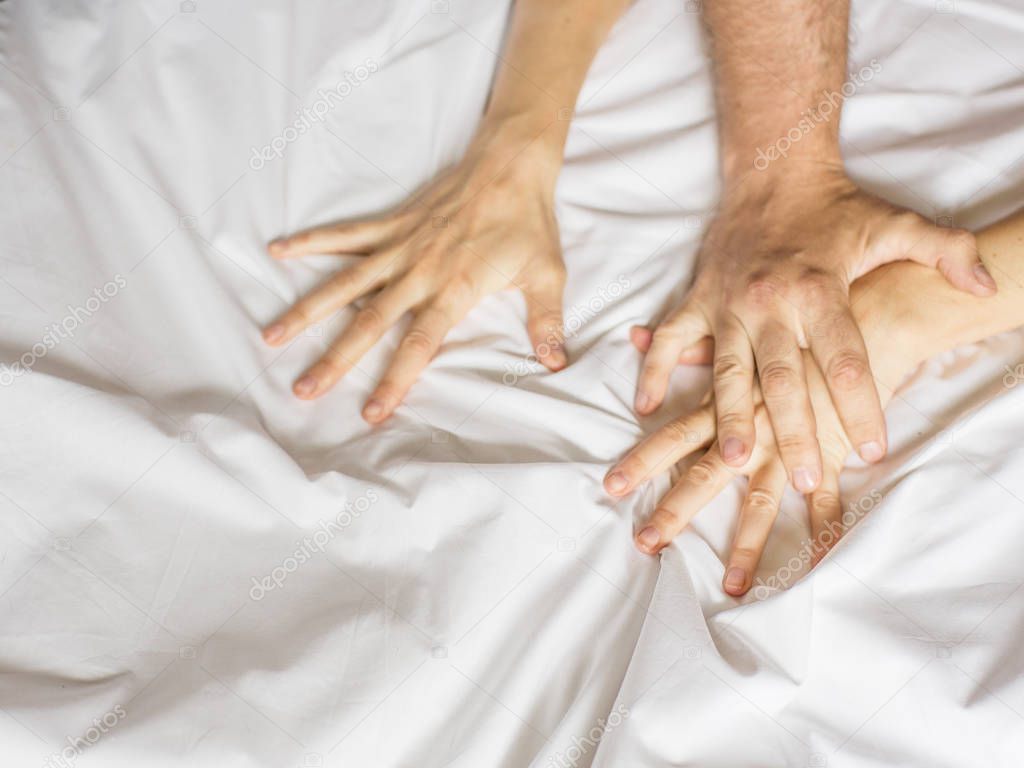 Couple having sex. Hand clutches grasps a white crumpled bed sheet in a hotel room, a sign of ecstasy, feeling of pleasure or orgasm.