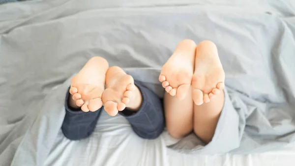 Las piernas de una joven pareja heterosexual relajándose en la cama. Enfoque selectivo, concéntrese en las piernas . — Foto de Stock