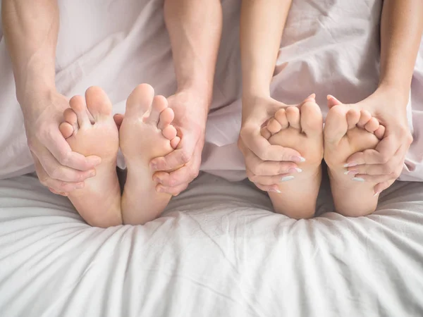 Echtpaar in bed. Een man en een vrouw houd hun voeten met hun handen. — Stockfoto