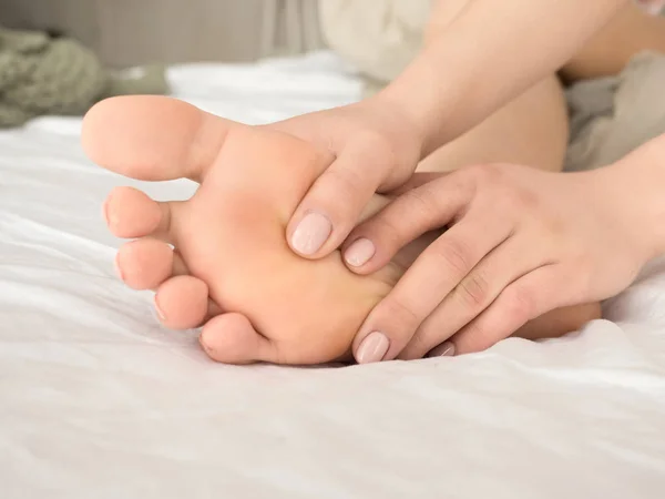 Woman massaging her tired feet on the bed. close up view. — Stock Photo, Image