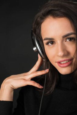 Yakın çekim müzik ve kulaklık koyu gri arka plan üzerinde tutan genç güzel esmer kadın portresi.