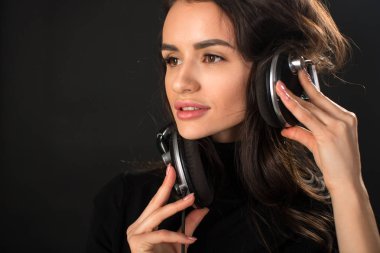 Yakın çekim müzik ve kulaklık koyu gri arka plan üzerinde tutan genç güzel esmer kadın portresi.