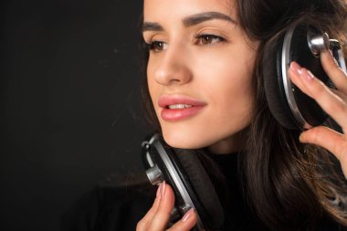 Yakın çekim müzik ve kulaklık koyu gri arka plan üzerinde tutan genç güzel esmer kadın portresi.