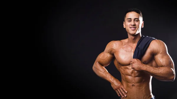 Homme bodybuilder fort souriant avec abdos parfaits, pectoraux, épaules, biceps, triceps et poitrine tenant une serviette. Isolé sur fond noir . — Photo