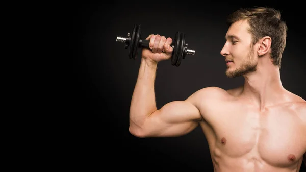 Lächelnder junger Mann beim Porträttraining mit Klingeln vor schwarzem Hintergrund. — Stockfoto