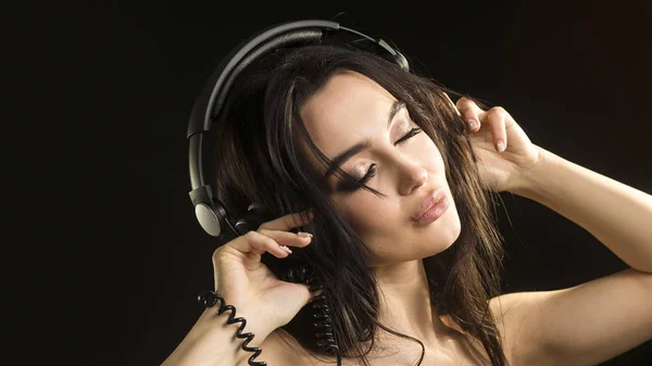 Portrait en gros plan d'une femme, qui écoute la musique dans un casque avec les yeux fermés sur fond sombre — Photo