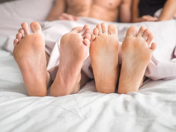 Close up of the feet of a couple on the bed. Loving couple is lying on bed under blanket.