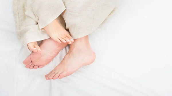 Feet of two couple sleeping on bed under blanket. Up view