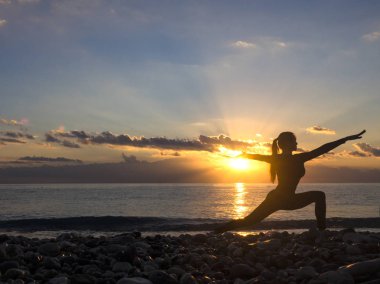 Oyun yoga egzersiz günbatımı veya gündoğumu zaman sahilde siluet kadındır.