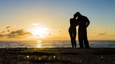 Sahilde romantik bir çift. Arka planda renkli bir günbatımı.