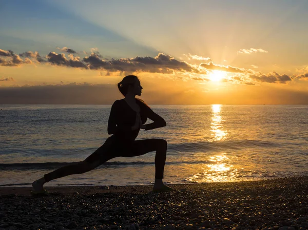 Silueta mujer es jugar ejercicio de yoga en la playa con la puesta del sol o la hora del amanecer . — Foto de Stock