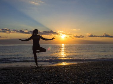 Deniz sahilde günbatımı sırasında yapıyor genç kadın silüeti. Yoga, fitness ve sağlıklı yaşam